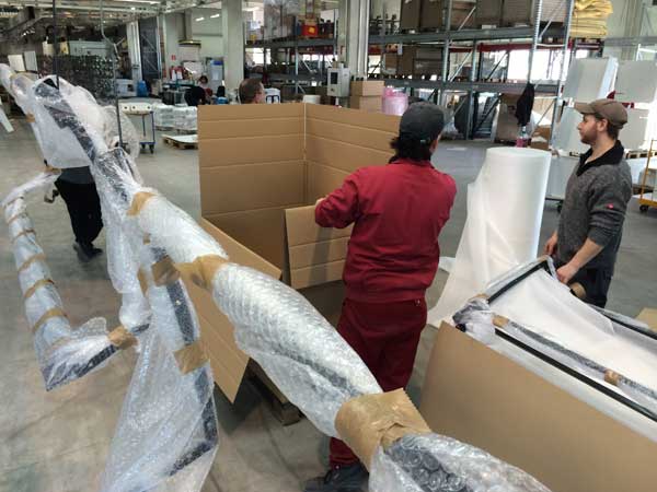 Große Produktteile werden von Mitarbeitern mit Luftpolsterfolie verpackt